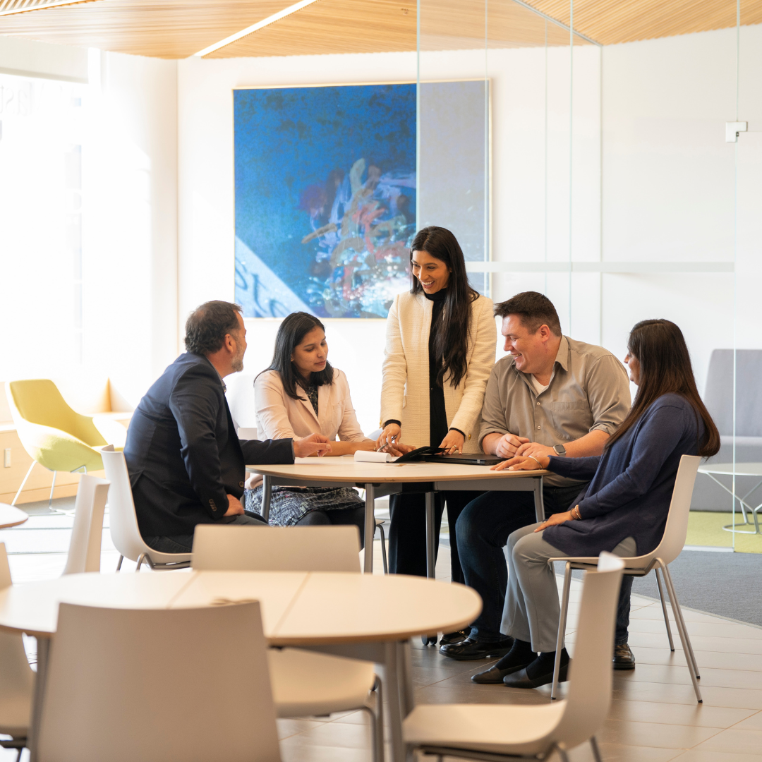 A smiling woman discusses the contents of a EMBA folder with four professionals.